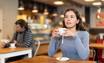 Portrait of young girl with cup in hands drinking coffee in coffee shop indoors