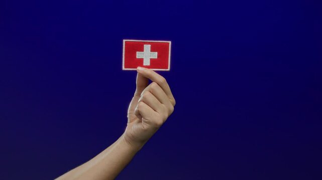 Man holding a swiss flag embroidery patch against a blue isolated background, capturing a symbolic gesture with focus on nationality and culture.