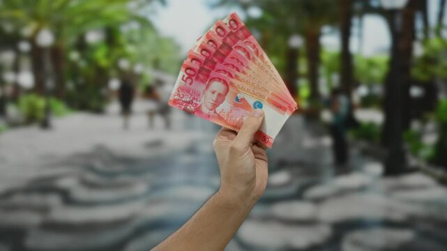 Caucasian man holds philippine pesos outdoors on a city street, showcasing vibrant filipino banknotes against a blurred urban setting, suggesting travel and financial themes.