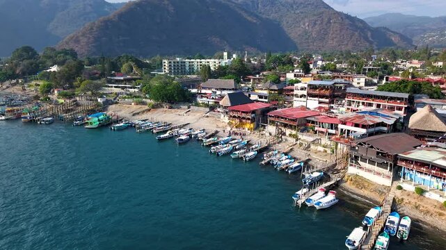 Beautiful cinematic aerial view os the Panajachel town surrounded by Toliman and Atitlan volcanoes, next to the Atitlan lake its piers and traditional fisher and tourist boats - Guatemala