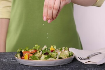 Woman salting tasty salad at dark textured table against white background, closeup