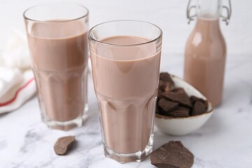 Tasty chocolate milk in glasses and pieces of chocolate on white marble table, closeup