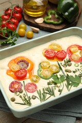 Raw focaccia with vegetables and spices on table, closeup