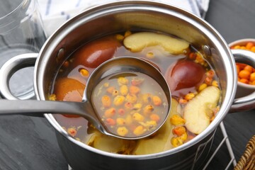 Taking tasty compot with ladle from pot on grey wooden table, closeup