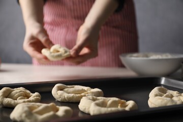 Woman putting salt onto raw pretzels at white table, closeup