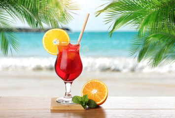 Refreshing cocktail on wooden deck under green palm leaves on tropical beach