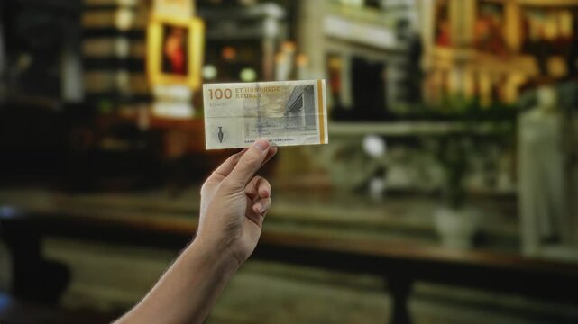 Man holding danish krone banknote outdoors in city street, highlighting currency and urban environment.