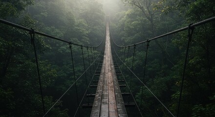 Wooden suspension bridge extending into a dense, misty forest with sunlight filtering through the canopy
