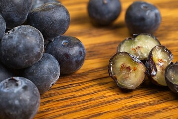 Close up of a pile of scattered blueberries on a wood table with some cut in half.