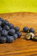 Pile of scattered blueberries on a wood table with a green background with some cut in half on a green background.