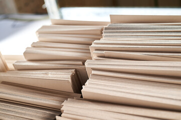 Stacks of thick paperboard ready for cardboard box production in a bustling factory environment