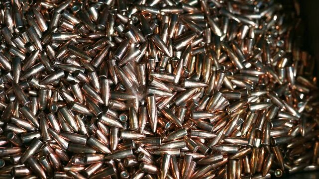 Shiny bullets fall down onto pile at manufacturing plant