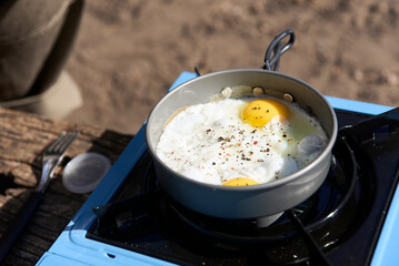 Making breakfast at a campsite: two eggs fried in a frying pan on a portable gas stove.