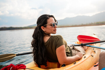 Latin hispanic young woman relaxing in a kayak on a serene lake, soaking up the sun and enjoying a peaceful summer vacation immersed in nature