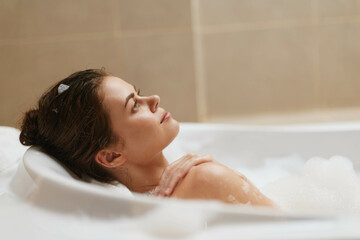 Obraz premium Relaxed woman enjoying a bubble bath, closed eyes and tranquil expression, surrounded by bubbles and soft lighting. Self-care and wellness concept.