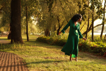 Young barefoot curly dark haired woman in green dress walking in the park