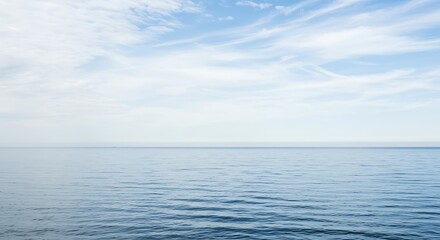 Fototapeta premium A serene and expansive view of a calm, blue ocean meeting a light blue sky dotted with wispy white clouds on a peaceful day.