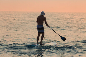 Male tourist paddleboarding through gentle waves at sunset near Agonda beach in South Goa, India