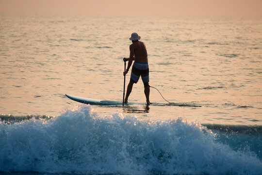 Male tourist paddleboarding at sunset near Agonda beach, South Goa, India