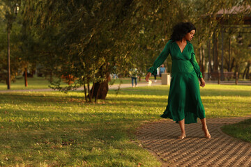 Young barefoot curly dark haired woman in green dress walking in the park
