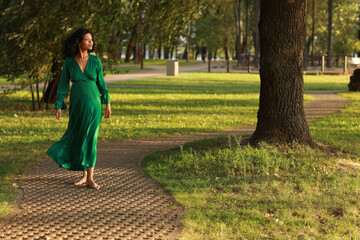 Young barefoot curly dark haired woman in green dress walking in the park