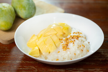 Sweet sticky rice with mango on wooden background. Mango is popular tropical fruit for dessert in Asia served with sticky rice, coconut milk. Selective focus and free copy space. Industrial food.