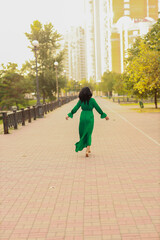 Curly dark haired woman in green dress walking in the street from back