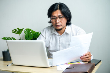 Middle-aged worker combining digital and physical tasks, analyzing documents beside his laptop.