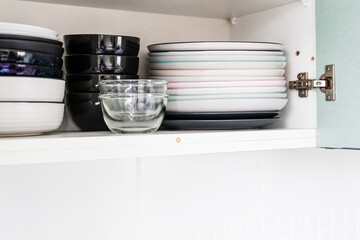 tidy decluttered kitchen cabinet shelves with plates and bowls neatly piled up, essential dinnerware and minimalist home organisation