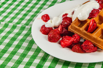 Delicious waffles with strawberries and cream on a plate