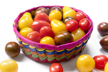 Bright and colorful assorted cherry tomatoes (yellow pear-shaped, red and black striped) in a vivid basket on the white background. Fresh organic garden produce.