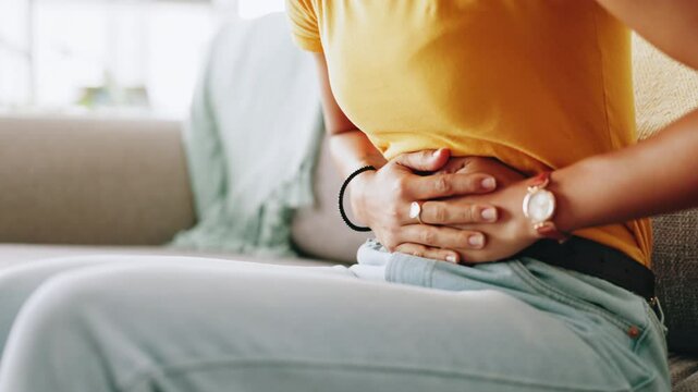 Hands, stomach pain and woman on sofa in living room of home for cramp, menstruation or pms. Abdominal, Indigestion and tummy ache with person in apartment for constipation, endometriosis or fibroids