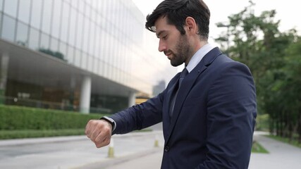 Skilled caucasian business man looking at time while standing at building. Attractive executive manager using smart watch while waiting for partner. Time management, punctuality concept. Exultant.
