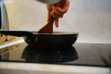 Cooking on a stovetop with wooden spoon and frying pan in kitchen