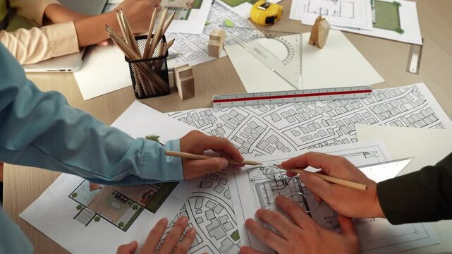 Smart architect and safety engineer discussion about building blueprint on table with architectural document, measurement tools and wooden block scatter around at modern office. Closeup. Delineation.