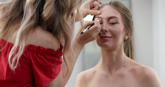 Woman professional make-up artist doing makeup of young girl model in beauty studio.