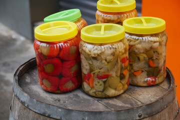 Vibrant jars of pickled vegetables on a wooden barrel in a market