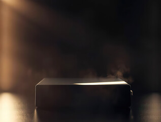 A small metallic box on a dark surface with a light shining on it from the side creating a warm glow