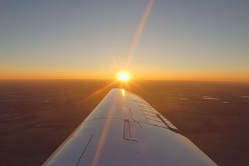 Aerial view of a sunset from an airplane, with wing in foreground.  A vast expanse of land stretches beneath, painted in warm sunset hues.  Sunlight beams through the airplane's wing
