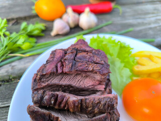 juicy steak on a white plate surrounded by vegetables.