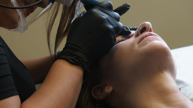 Esthetician gently uses a microblading brush tool on the client&rsquo;s eyebrow with Gloved hands, soft light, and close contact capture precision and calm in the beauty procedure in slow motion.