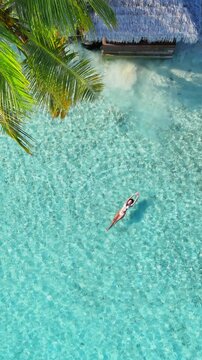 Calm vertical paradise aerial view, Tropical white sand beach with turquoise water and palm trees, woman floating, swimming, serene atmosphere for summer travel, hotel, resort, family vacation