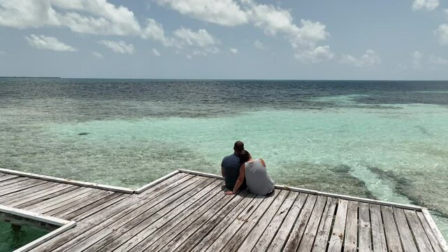 Behind passover aerial view of couple sitting on pier overlooking the Caribbean.