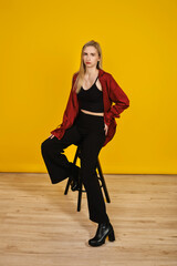 Stylish model poses confidently on a stool against a vibrant yellow backdrop