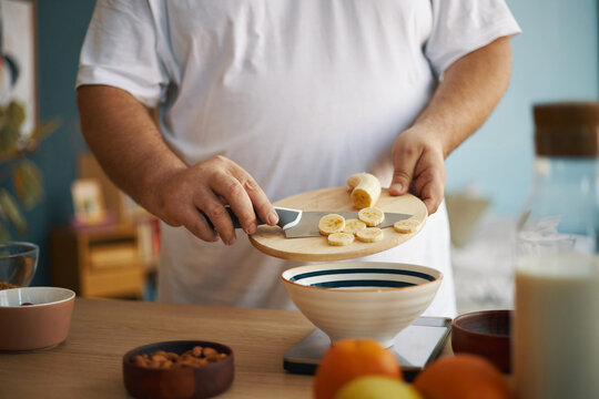 Man slicing bananas on cutting board in kitchen while preparing breakfast, with focus on hands and food