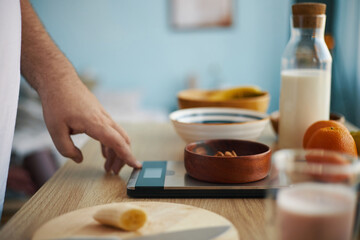 Close-up image showing hand measuring various ingredients on digital kitchen scale, including...