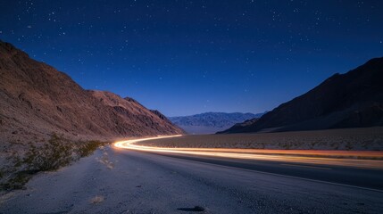 A nighttime view of a winding road through a desert landscape under a starry sky.
