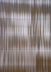 abstract blur monotone background of white or off white curtains in window with light coming in blurred by intentional camera movement and long time exposure making wavy like moving up and down lines