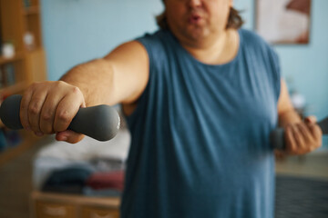 Close-up of individual lifting dumbbells in a room with bright natural light, showcasing focus on...