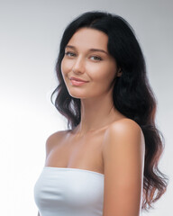 Portrait of a young Caucasian woman with long dark hair and smooth, glowing skin, wearing minimal makeup and a strapless top. Ideal for beauty, skincare, and wellness concepts.